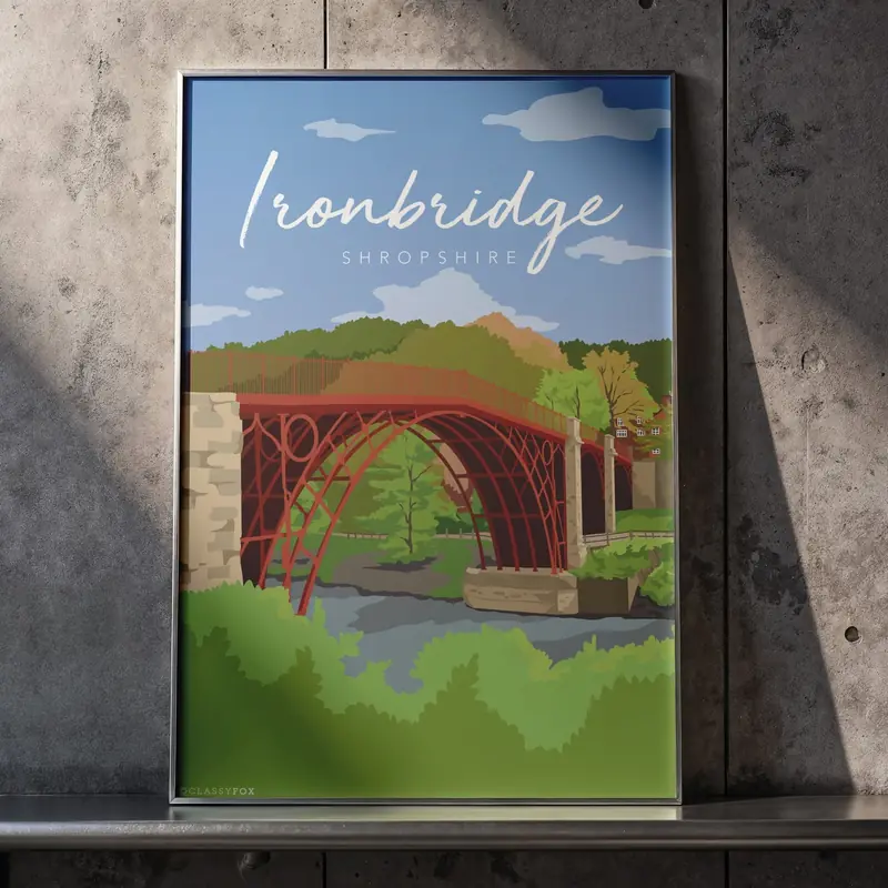 A framed illustrated travel poster leaning against a concrete wall, showing the red iron arch of the Ironbridge over the river with wooded hills behind, and the word Ironbridge in white brush script above the word Shropshire.