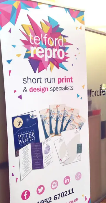 A Telford Repro pull up banner standing in their showroom, printed with the shard logo and the words short run print and design specialists, with a rack of sample cards beside it.