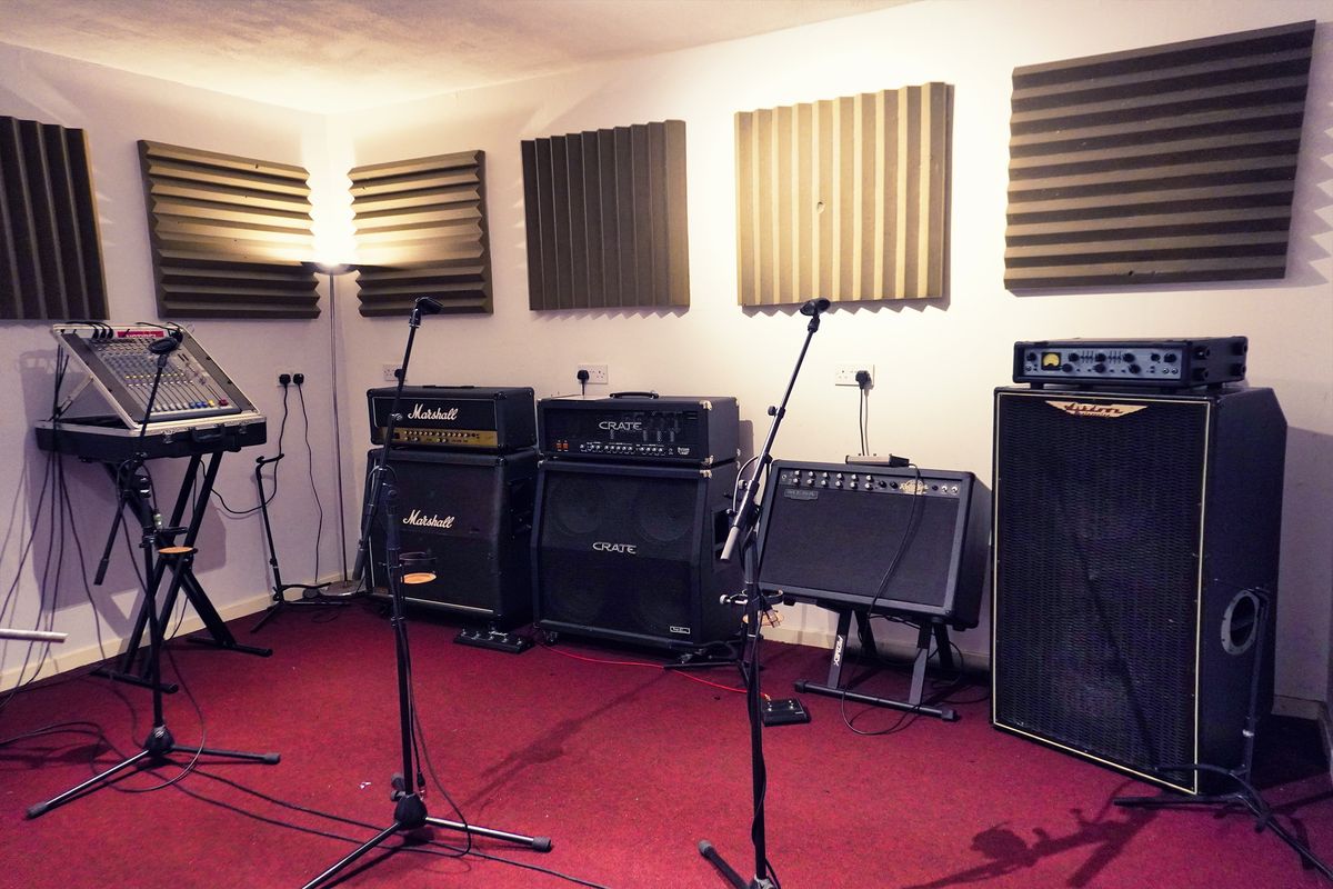 A Smash Room rehearsal room lit by warm lamplight, red carpet, grey acoustic foam and a stack of Marshall and Crate amplifiers