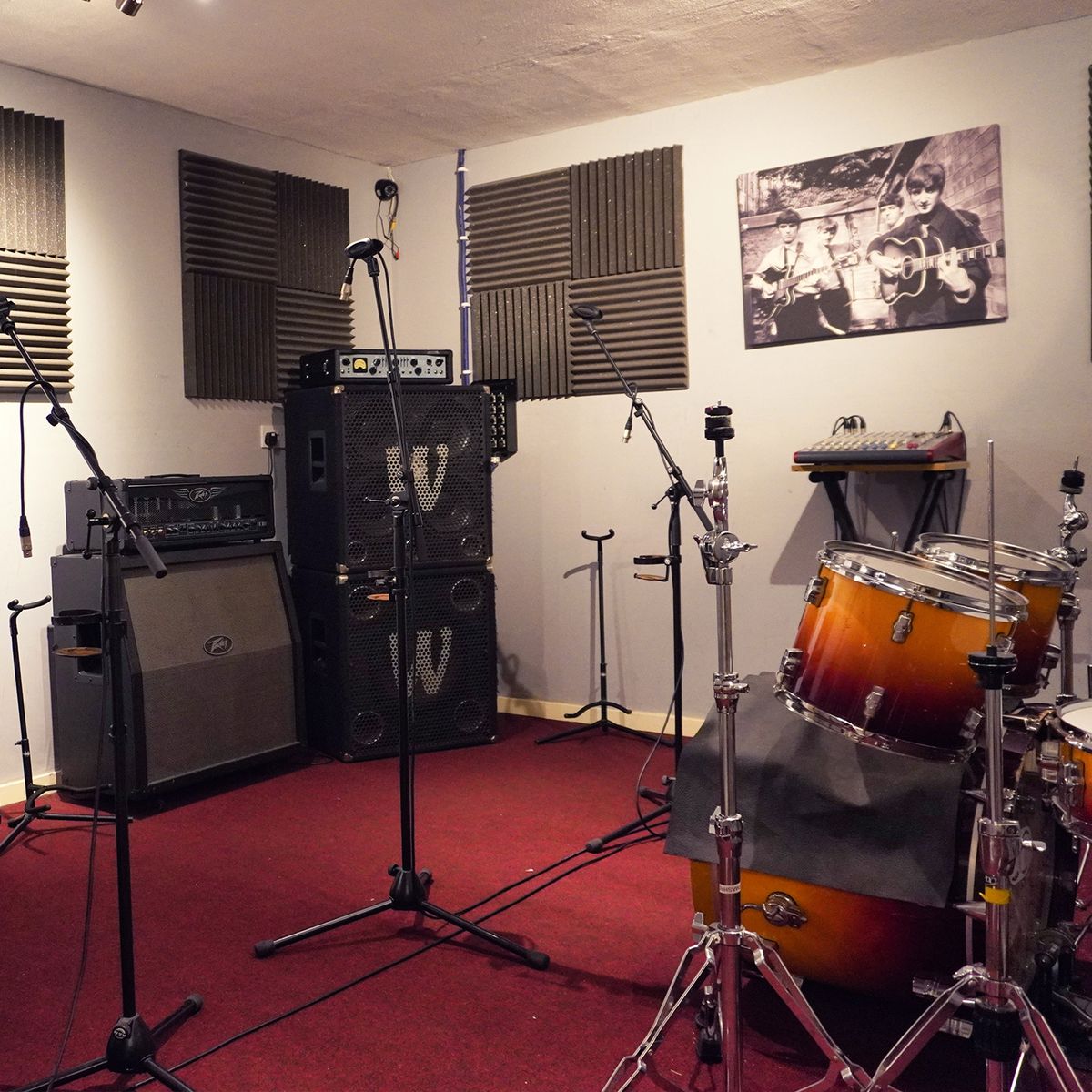 Rehearsal room with a sunburst drum kit, bass cabs and a Beatles canvas on the wall