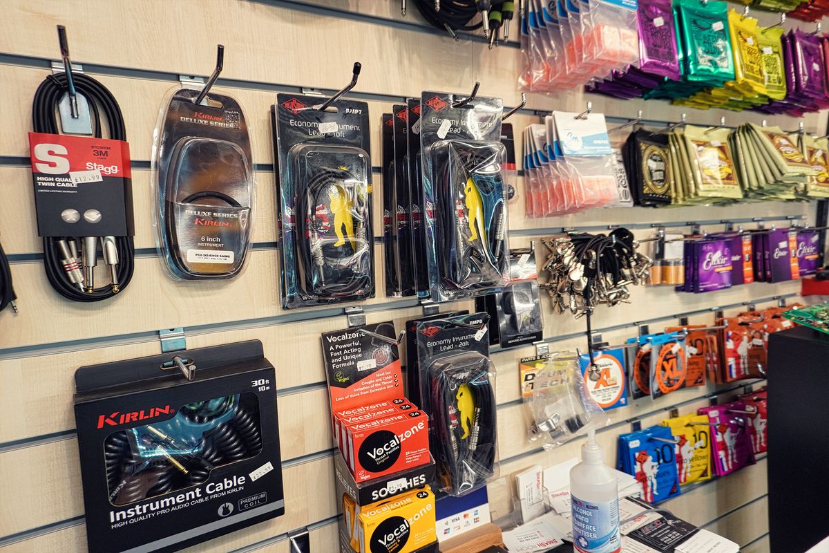 A wall of the music shop hung with instrument cables, guitar strings in colourful packs and accessories