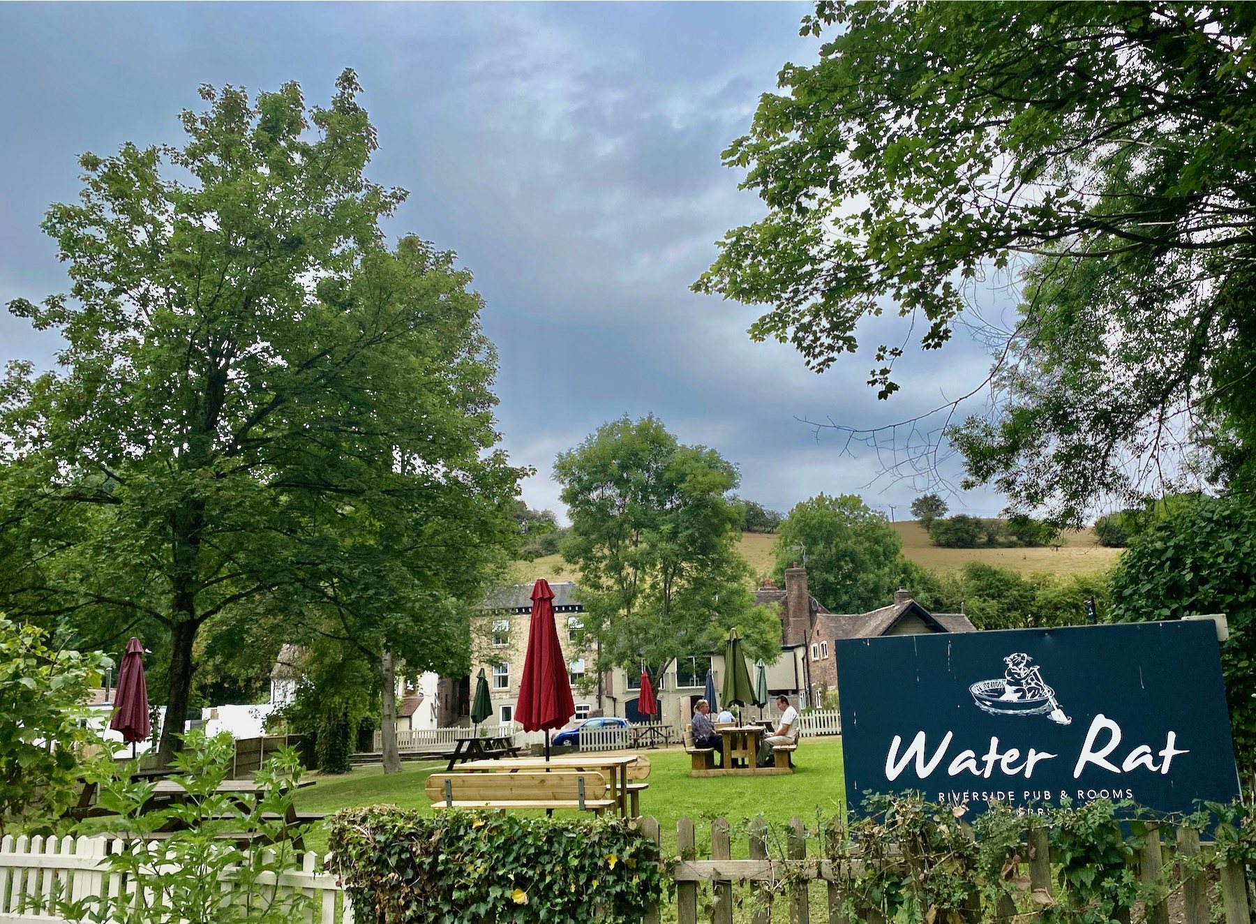 The riverside beer garden at The Water Rat with red parasols and seating on the lawn
