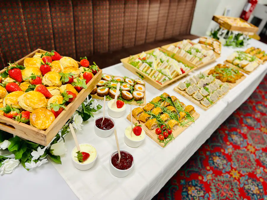 An afternoon tea spread of finger sandwiches, fruit and desserts with strawberry conserve