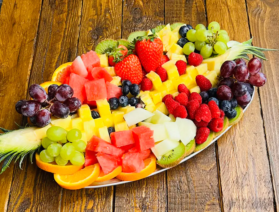 A fruit platter of watermelon, strawberries, grapes, kiwi and melon on a dark wooden board
