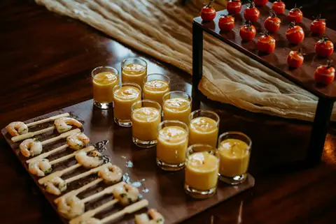 Gazpacho shot glasses lined up beside breadsticks on a dark table