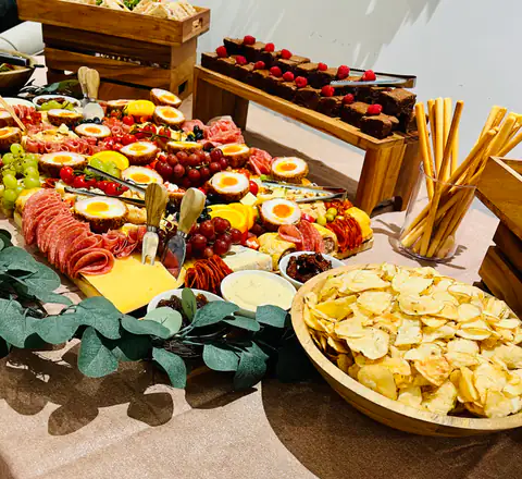 A graze table with a bowl of crisps, breadsticks and salami, framed by trailing eucalyptus