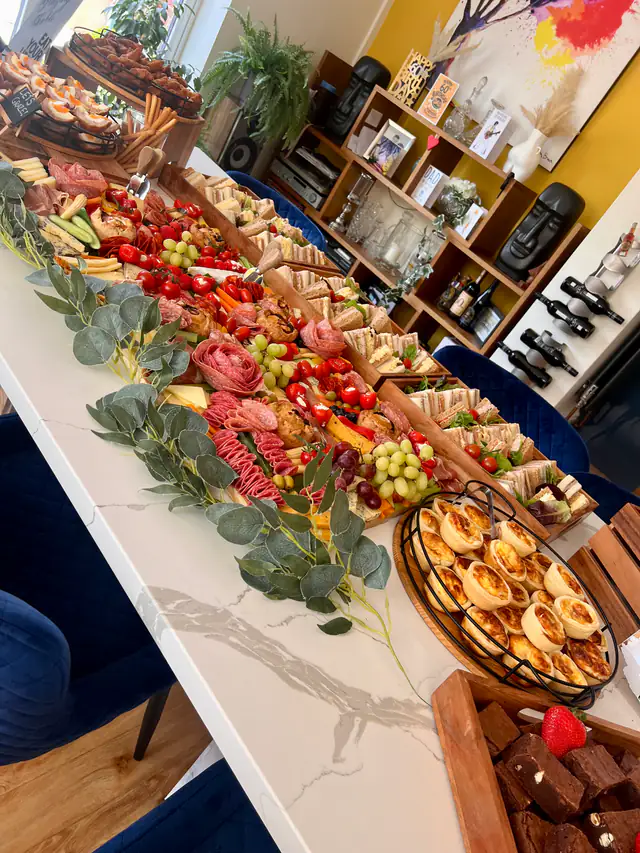 A long grazing table dressed with eucalyptus, strawberries, grapes and chorizo roses down the centre