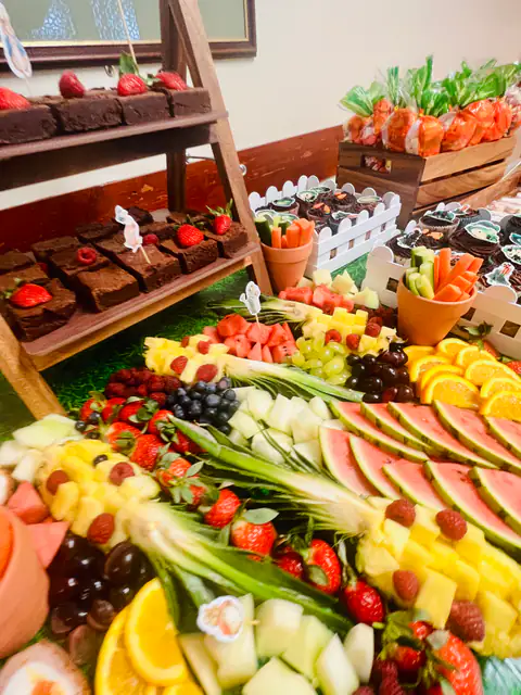 Sliced melon, grapes and berries fanned across a grazing table beside brownies