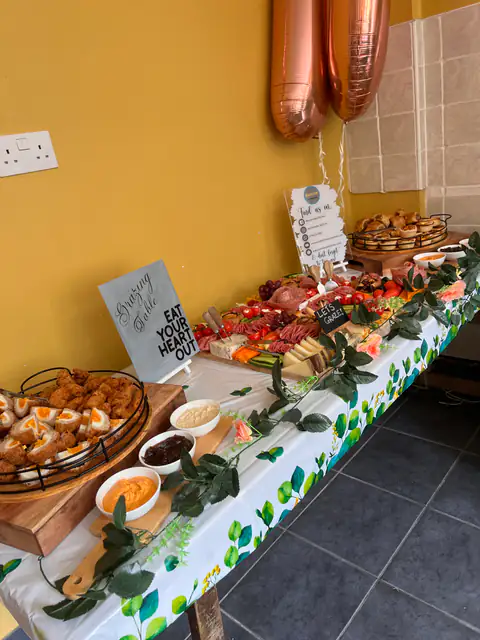 A grazing table set along a village hall wall with a chalkboard sign and foliage runner