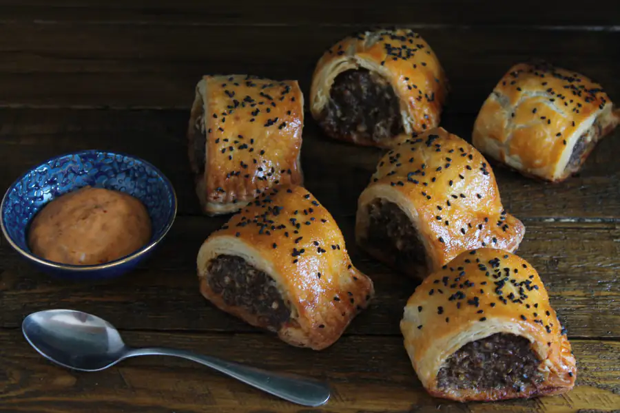 Homemade puff pastry sausage rolls topped with black sesame seeds, on dark wood